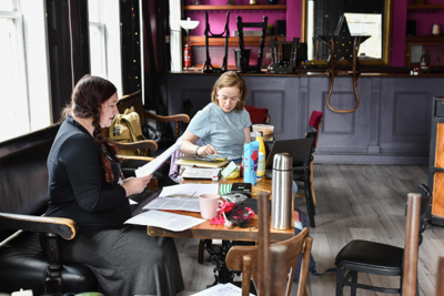 Two members of Blue Fire Theatre Company sitting around a table in a bar or cafe. The table is covered with notes.